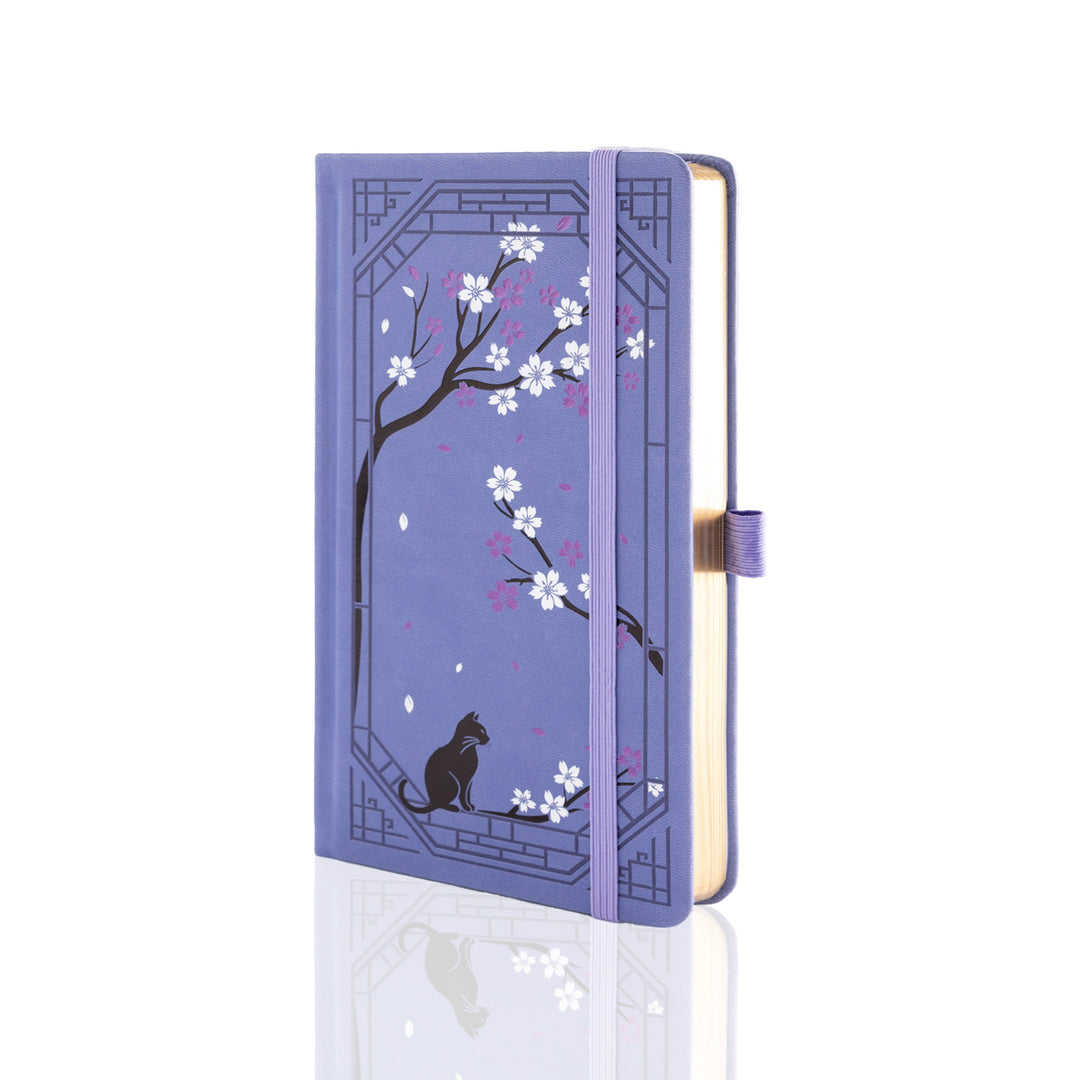 A purple hardcover notebook with an illustrated design of a black cat under blooming cherry blossom trees, shown on a clean white background with a soft reflection.